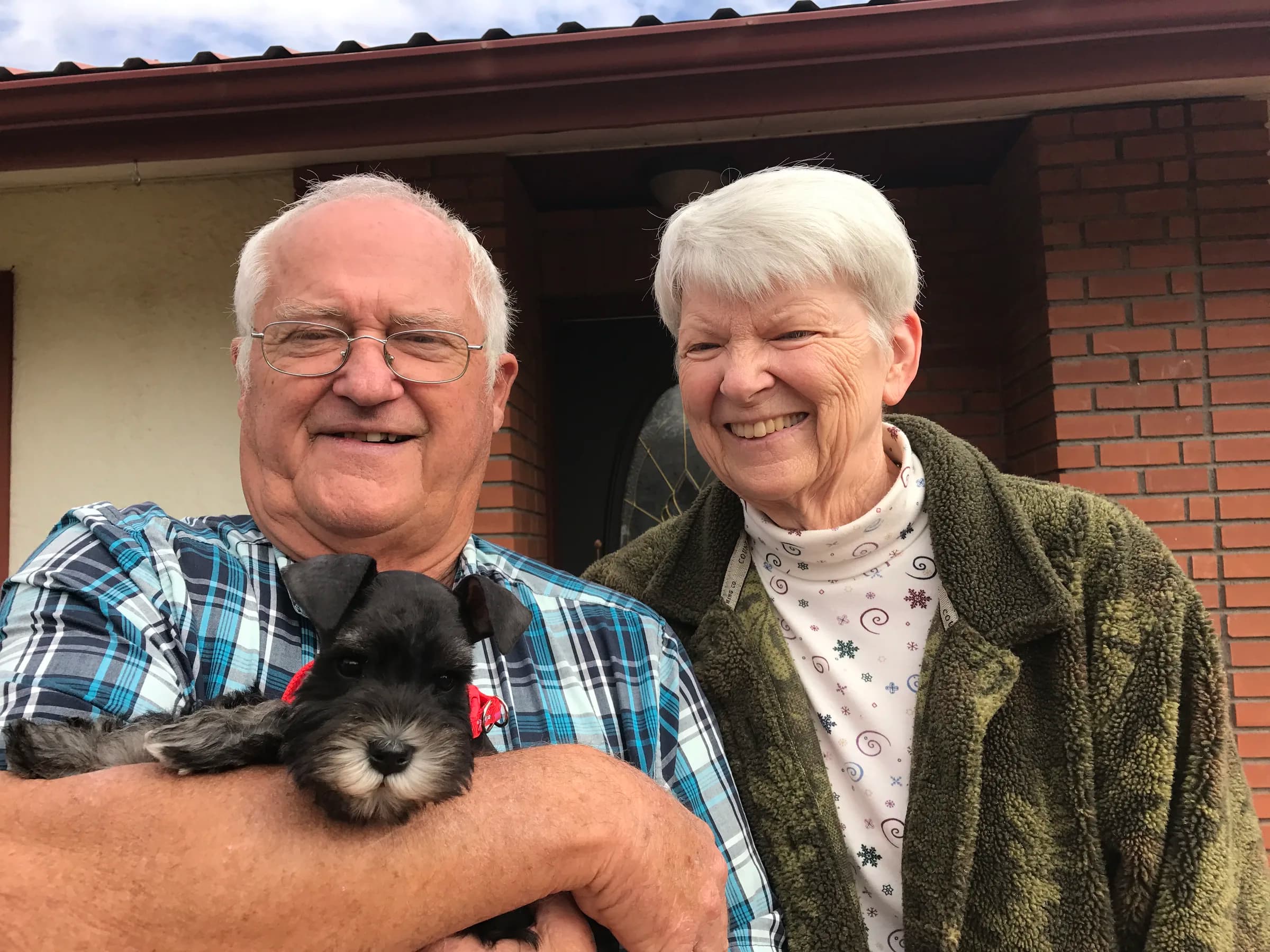 A couple on their porch holding a miniature schnauzer puppy