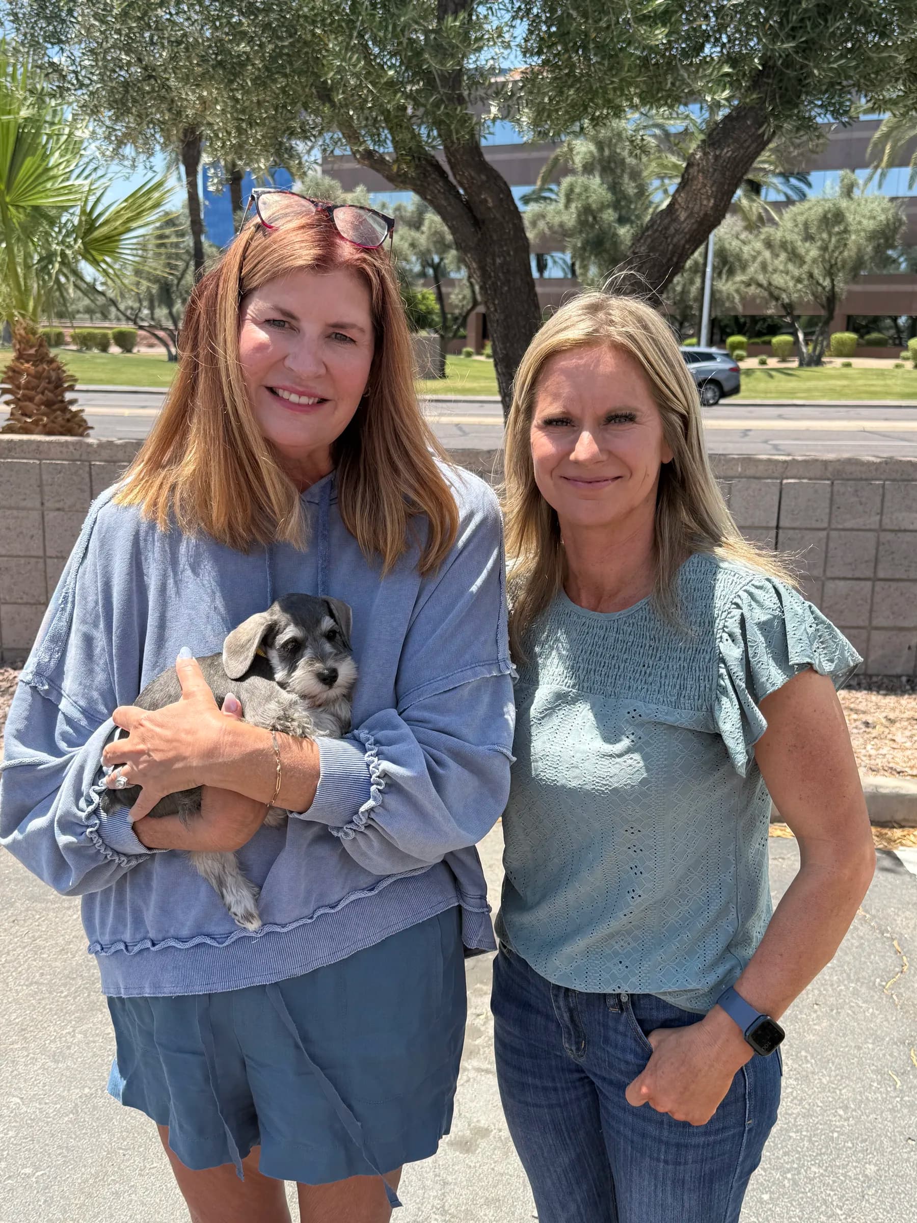 Two women holding a miniature schnauzer puppy in a parking lot